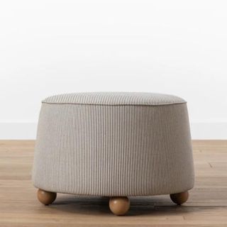 A small ottoman with subtle stripes and spherical wooden feet