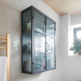 Black wall cabinet with fluted glass doors in a bathroom with bare plaster walls