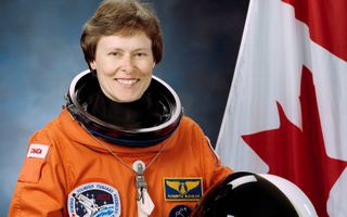 Roberta L. Bondar wearing an orange flight suit stands next to the Canadian flag.