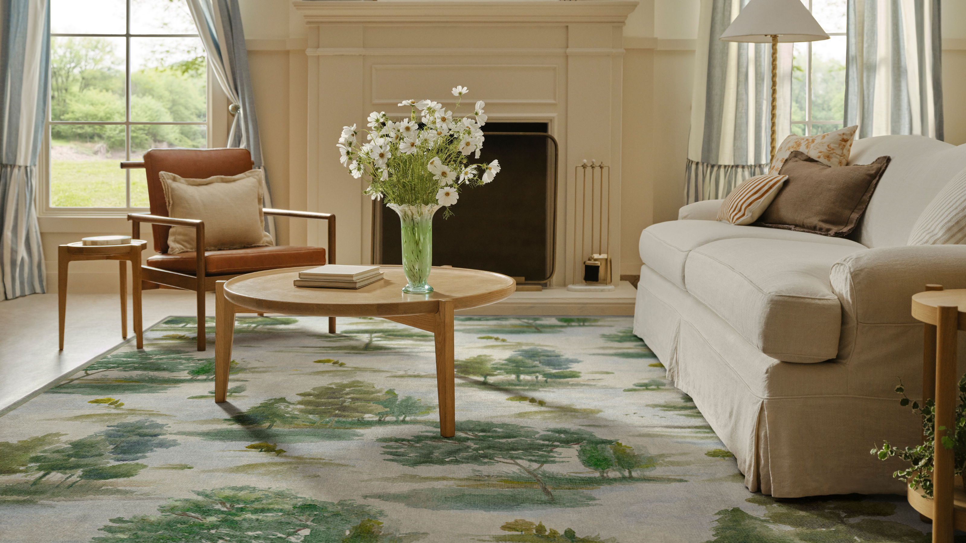 a living room with a pastoral scene rug, a coffee table, a cream sofa, and a large fireplace 