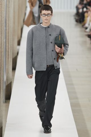 Miu Miu model wearing a gray cardigan, black trousers, and glasses at the fall/winter 2023 show.