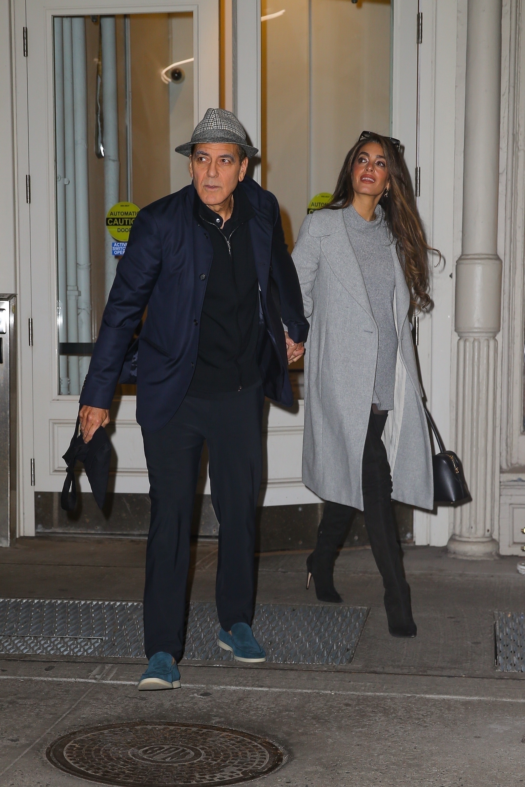 George and Amal Clooney hands in New York City, while Amal Clooney wears a sweater dress and thigh boots