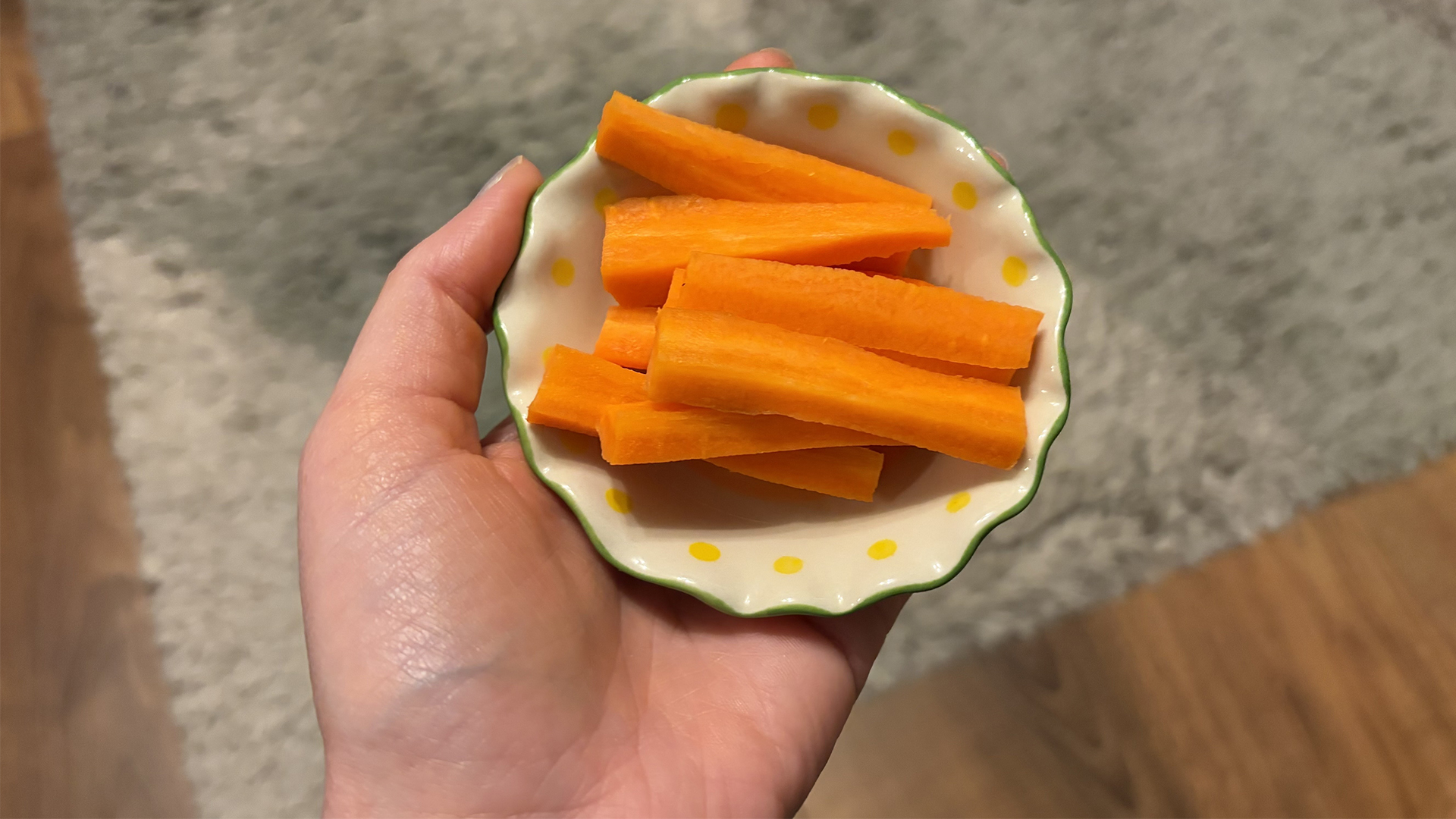 A close up of a hand holding a small bowl with slices of carrot in it