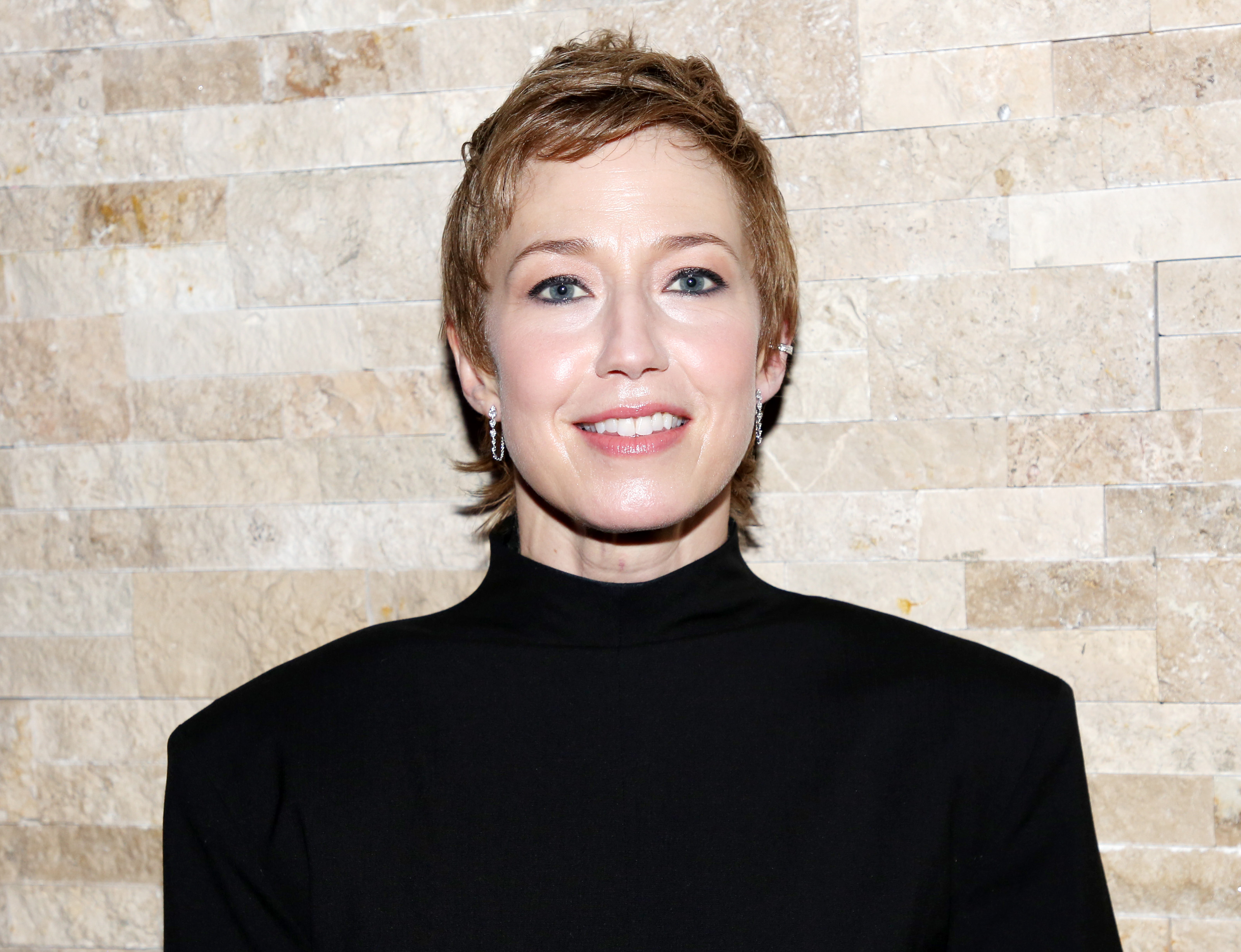 a white woman with short, brown hair poses in front of a stone wall