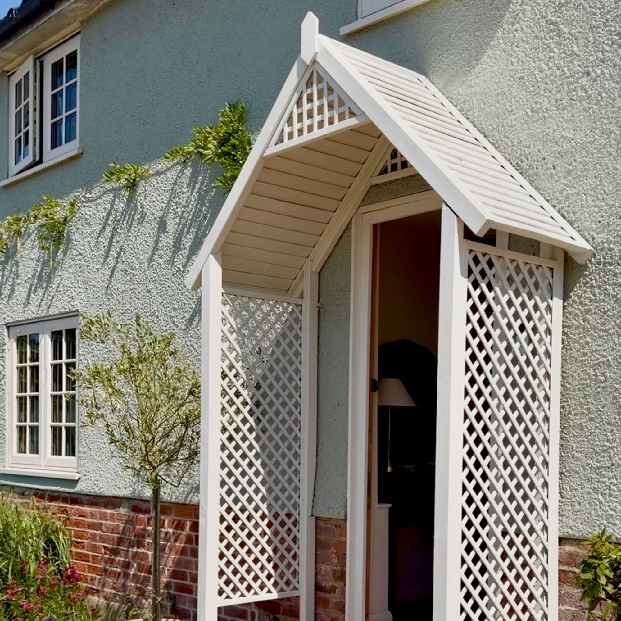 Green painted house with brick base and cream painted windows, door frame and latticed porch
