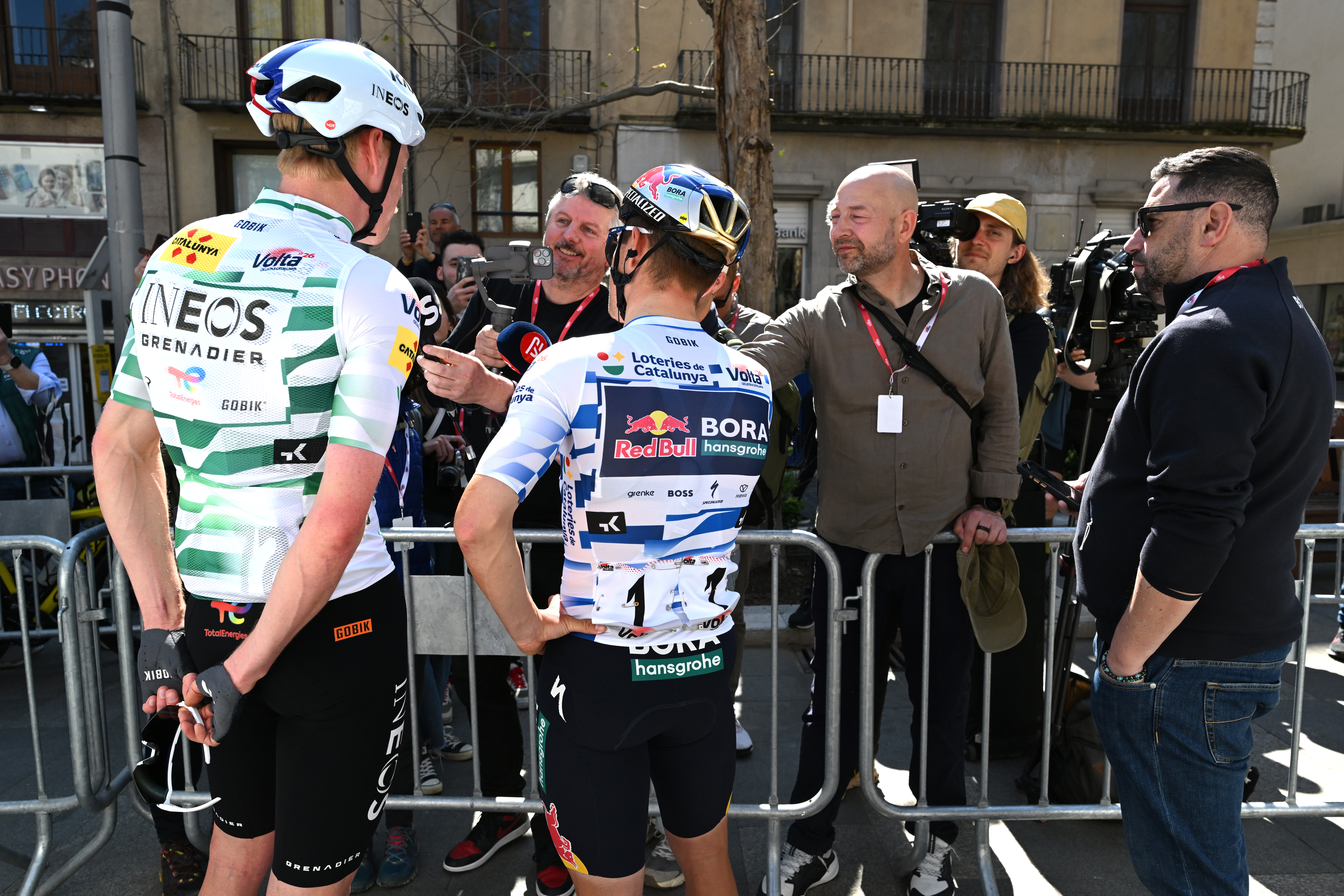 Dorian Godon (left) and Remco Evenepoel (right) face away from the camera as they talk to journalists before the start of stage 2 at the Volta a Catalunya 2026.
