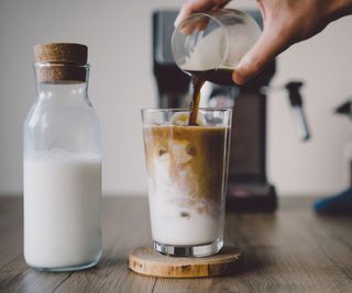 A coffee smoothie on a countertop with milk in a jug beside it