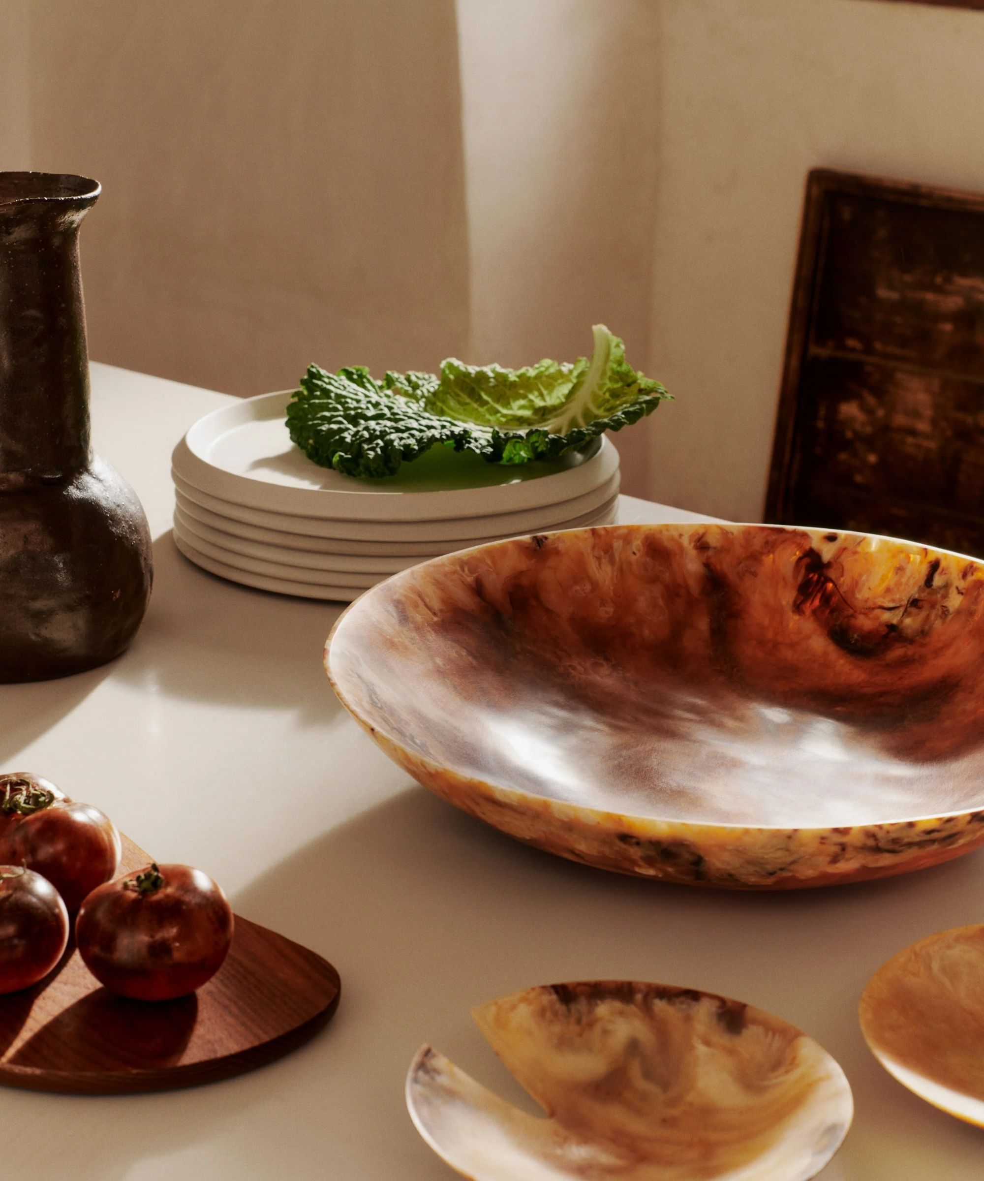 Resin serving bowl next to resin serving spoons and a stack of white stoneware plates