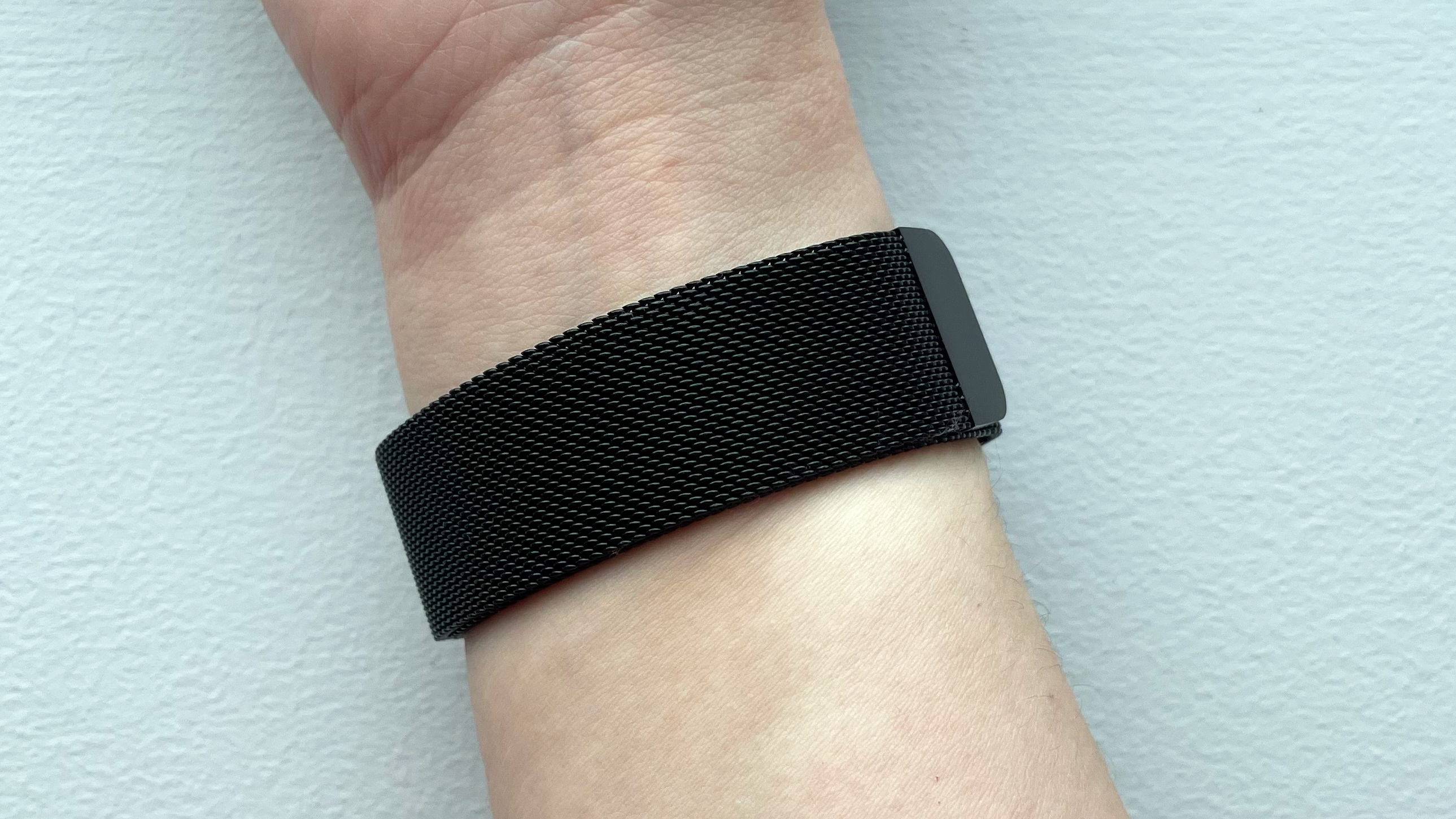 A black-coloured metal mesh watch strap wrapped around a woman's wrist.