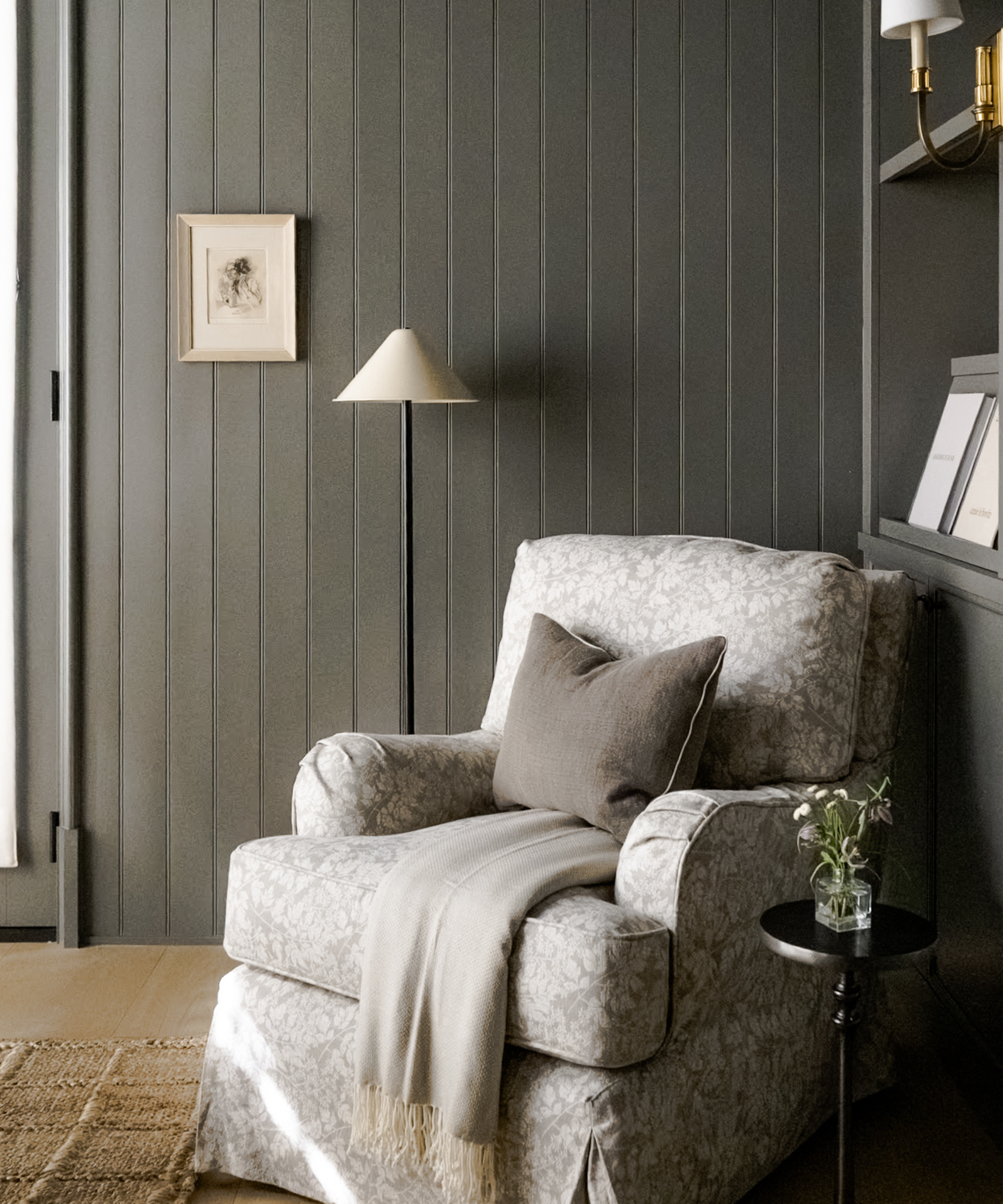 a cozy gray armchair with a pillow and a blanket and a floor lamp in a room with dark gray painted walls