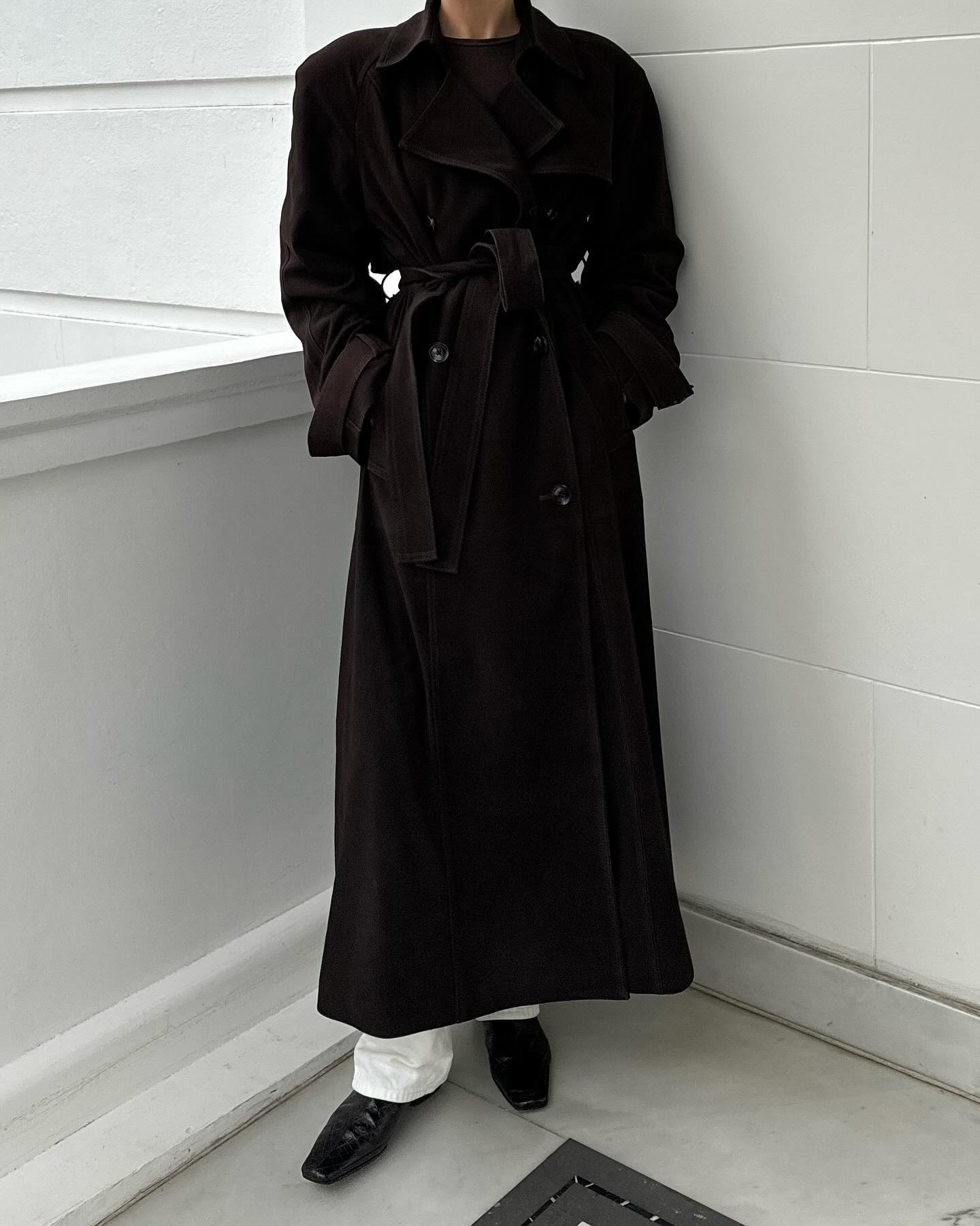 A woman wears a long trench coat, white jeans, and black croc-embossed boots.