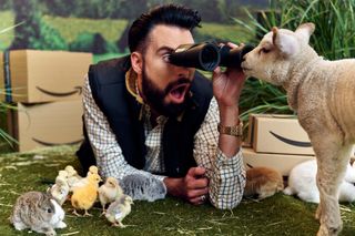 Rylan holding looking at a goat directly in front of him through binoculars surrounded by Amazon parcels and chicks