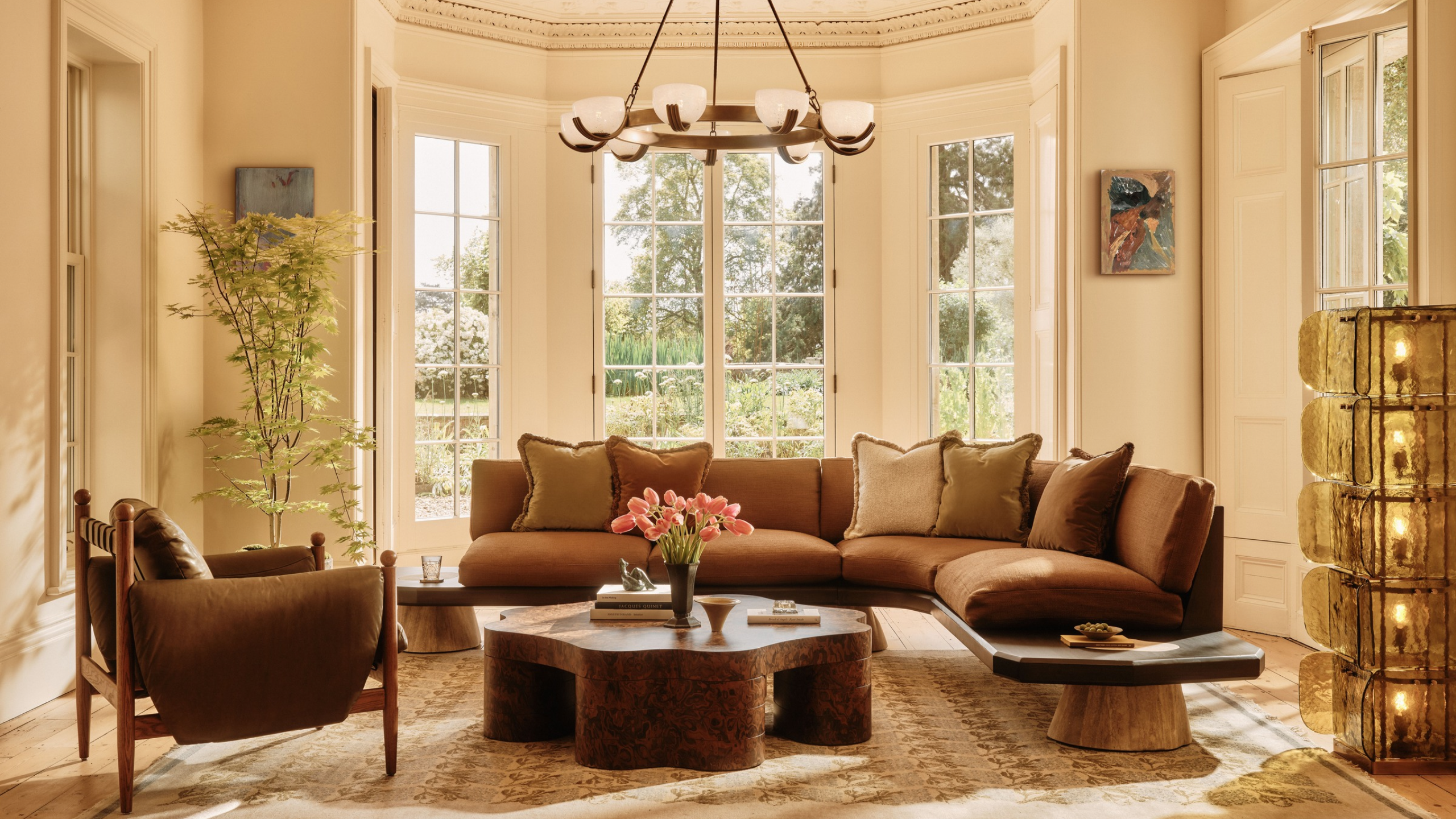 A bright living room with a round chandelier, a textured glass floor lamp, and brown furniture