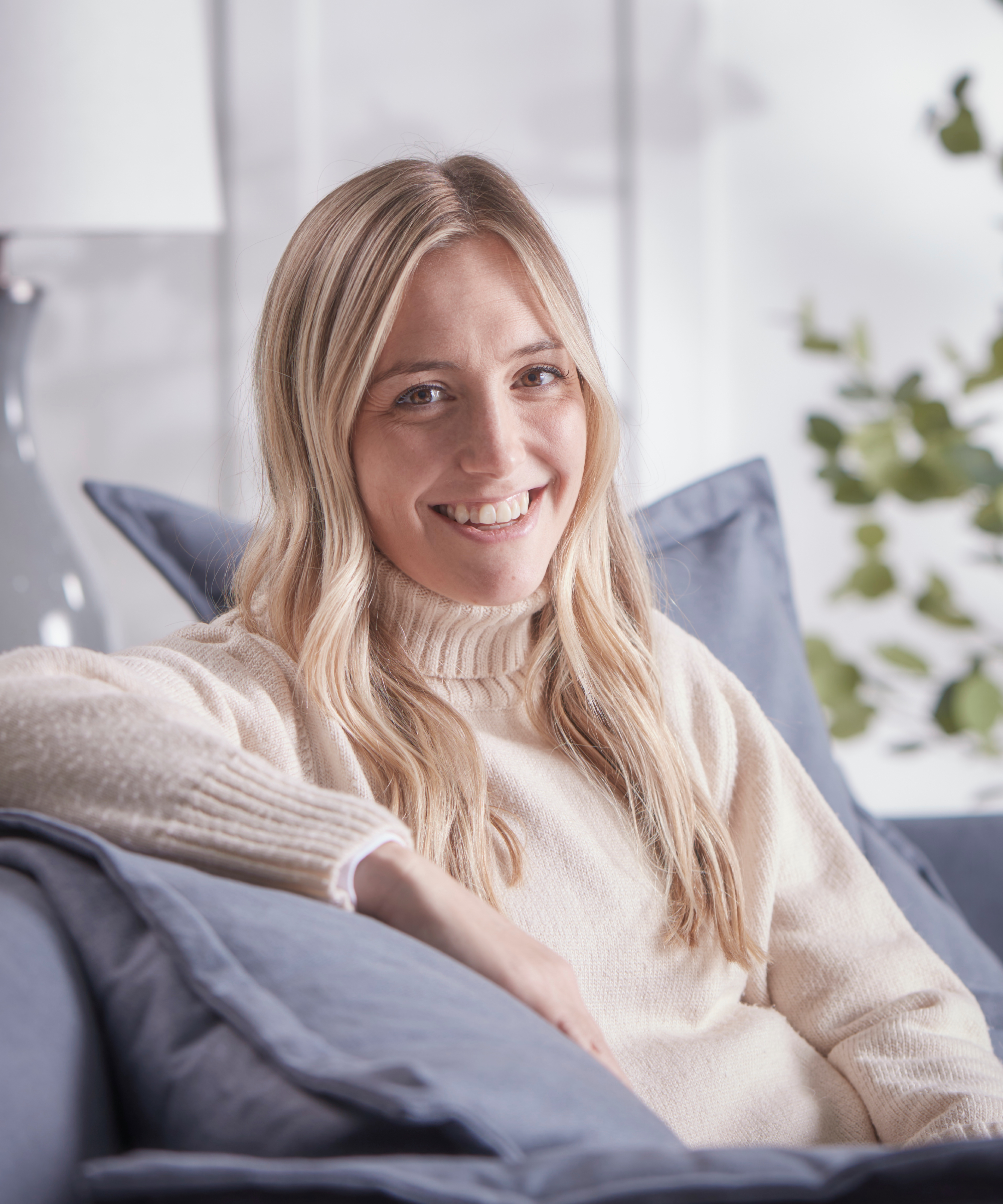 headshot of female sat on sofa with long blond hair wearing cream jumper