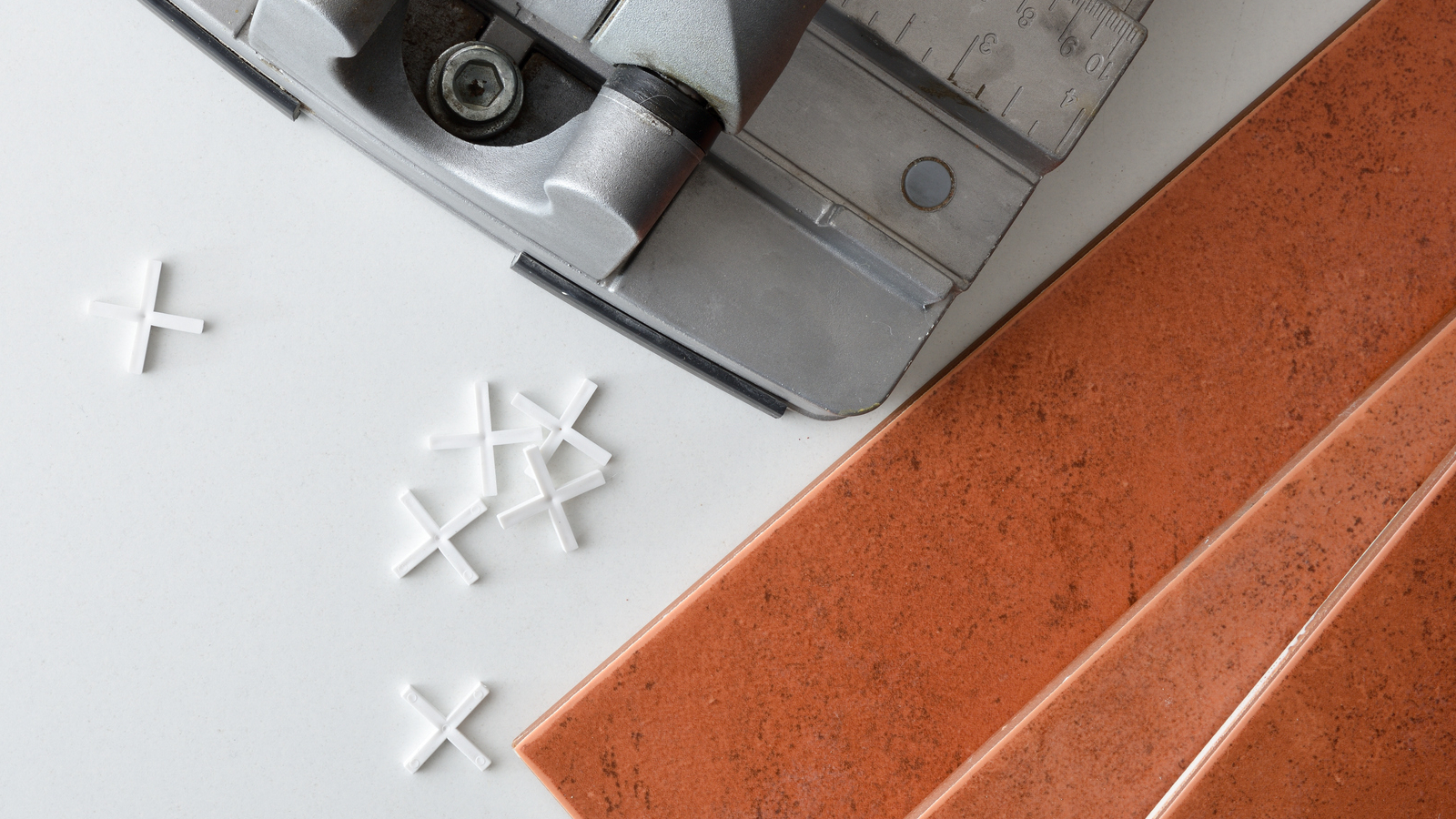 Cross-shaped tile spacers laid out next to a tile cutter and some terracotta tiles