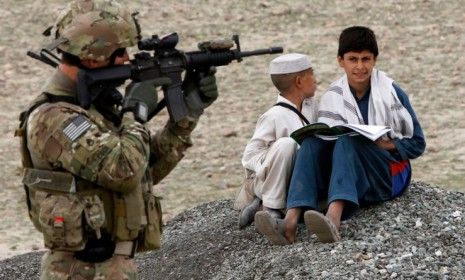 Afghan residents sit on the ground near a U.S. Army soldier securing the permitter of a government building in Laghman province on March 25.