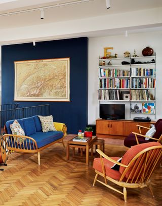 An open-plan living room with blue living room paint color idea as a feature wall, with a wooden floor and book shelves to the right