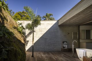 bathroom that opens to courtyard against concrete wall and tropical foliage