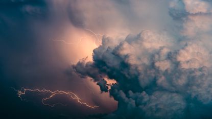 Storm clouds with the sun behind them and showing lightning.