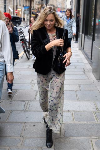 Kate Moss wears a velvet blazer, a sheer floral maxi dress, black boots, and a black handbag.