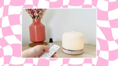 Best essential oil diffusers: Neom diffuser in room with pink vase and hand holding a remote, on pink checkered warped background
