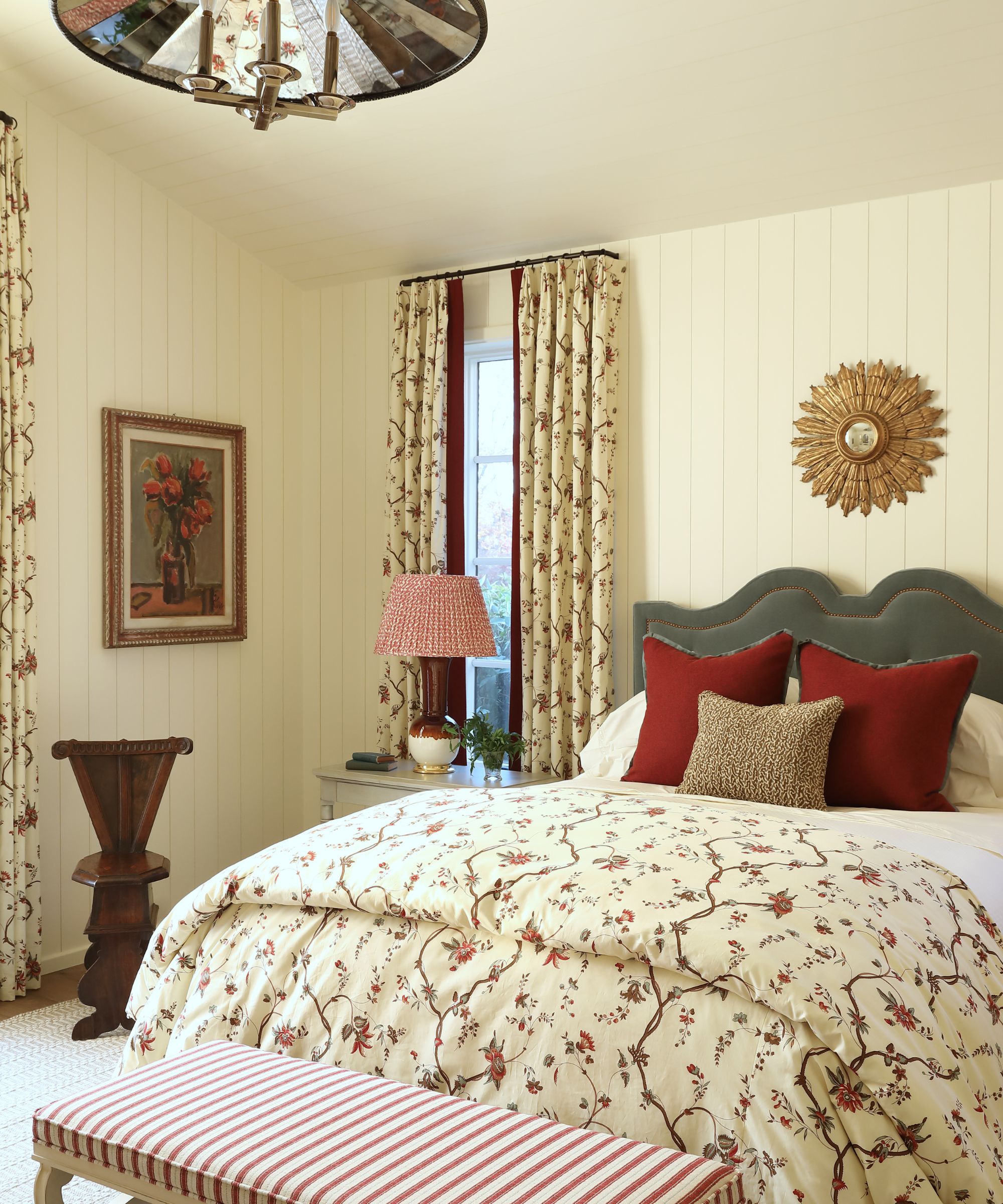 Vintage bedroom with cream shiplap walls and painted ceiling, floral curtains, double bed with floral throw and striped bench