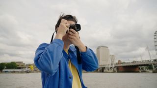 Man in blue shirt looking through lens of camera