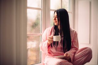 A happy woman wearing pink pyjamas while holding a mug.