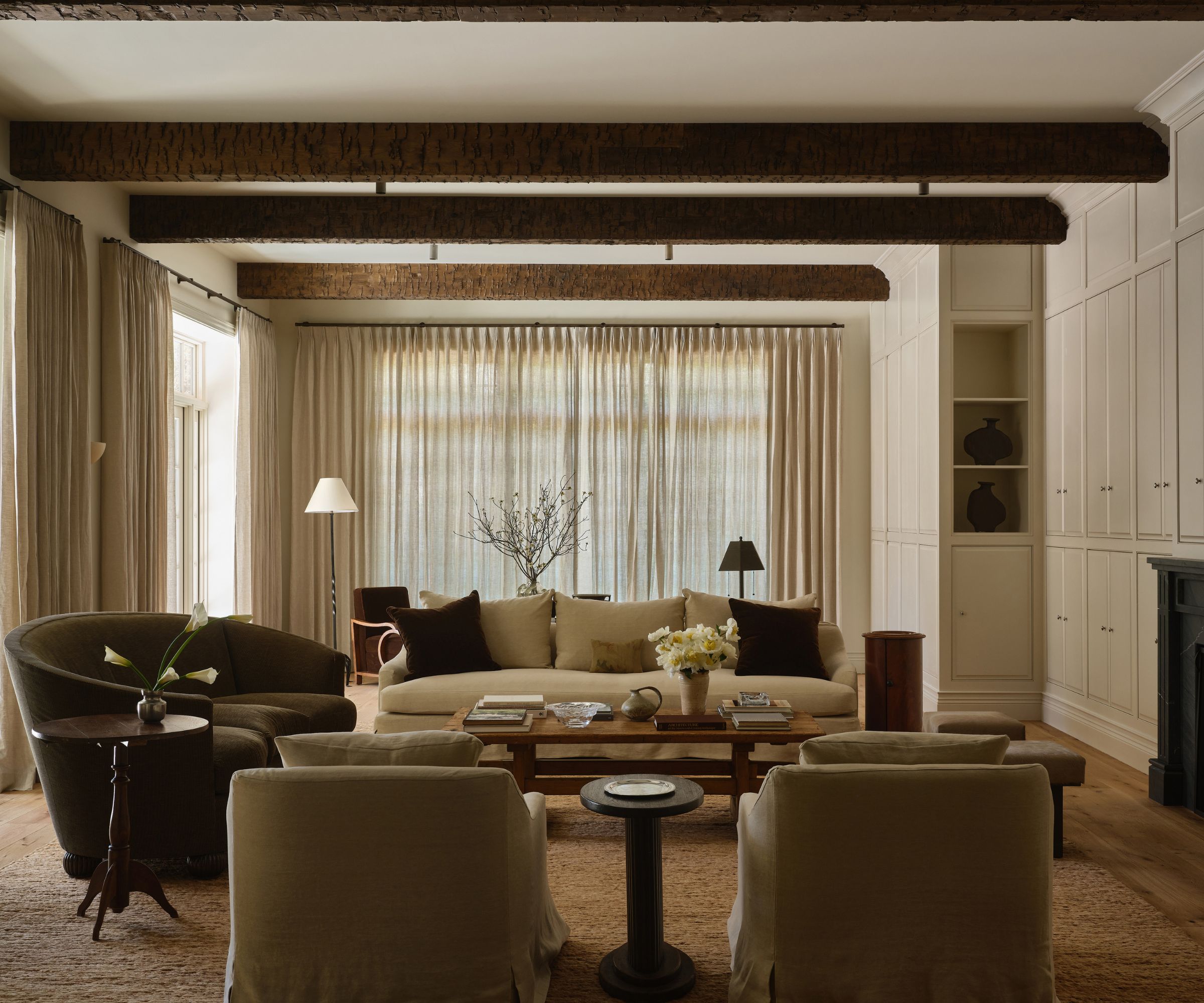 Cozy neutral living room with beamed wooden ceiling, sofa and armchairs surrounding a coffee table