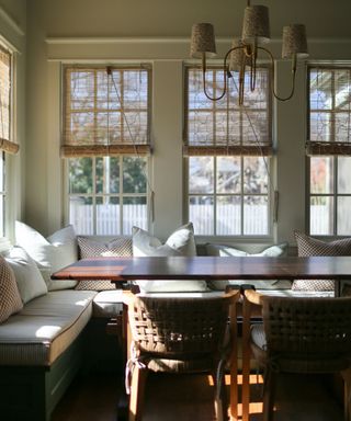 breakfast nook with a banquette with cushions and a large table, four windows with chik blinds