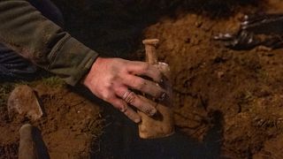 A hand holding a glass bottle that has been dug out of a hole in the ground