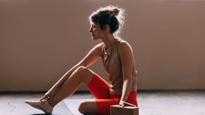 A woman on her phone in gym wear prior to doing some of the best Pilates exercises