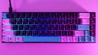Top-down view of the Razer Reclusa X Mini 65% gaming keyboard illuminated with vibrant RGB backlighting under ambient purple light.
