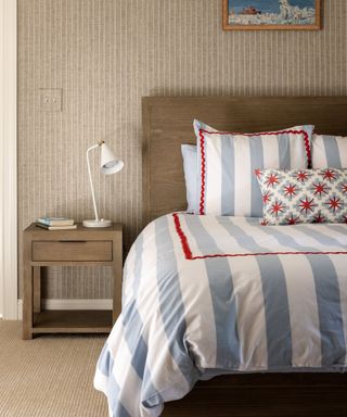 Bedroom with neutral stripped wallpaper and blue, white and red bedding