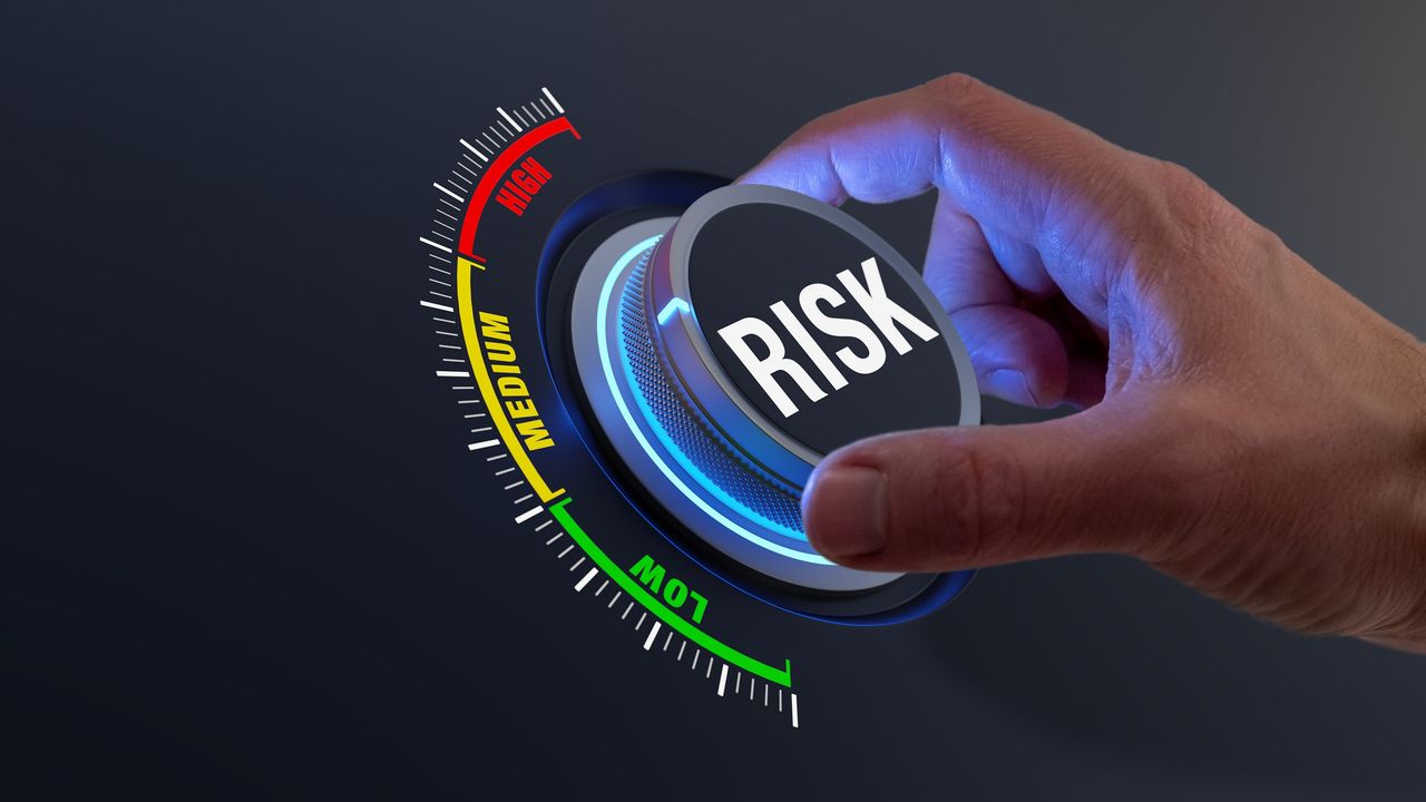 A man&#039;s hand turns a dial labeled risk.