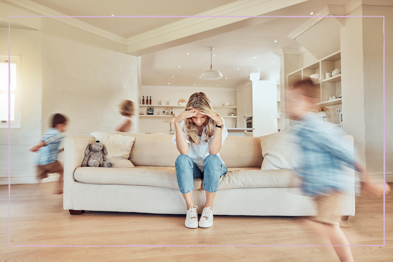 Stressed mother sitting on the sofa while her children run around the living room