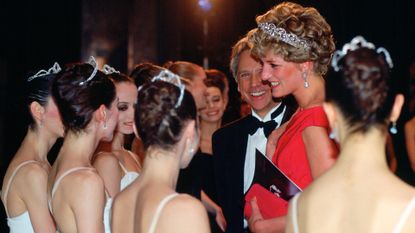 Princess Diana wearing a red gown and tiara talking to ballet dancers