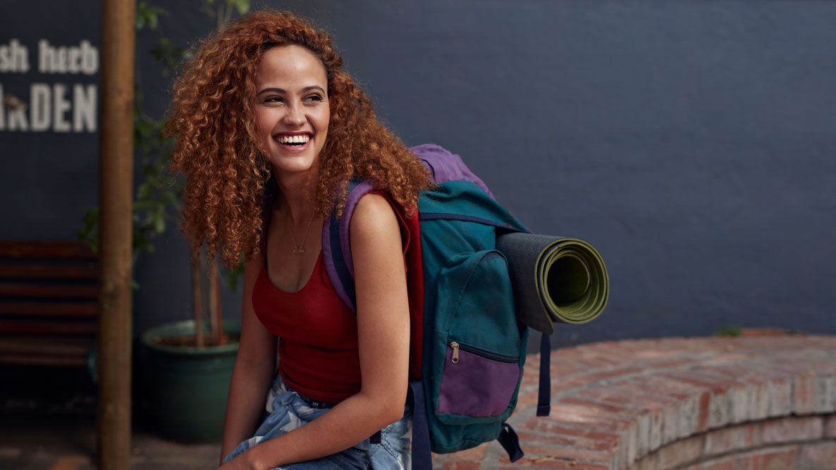 Image shows a woman smiling, carrying one of the best travel backpacks.