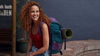 Image shows a woman smiling, carrying one of the best travel backpacks.