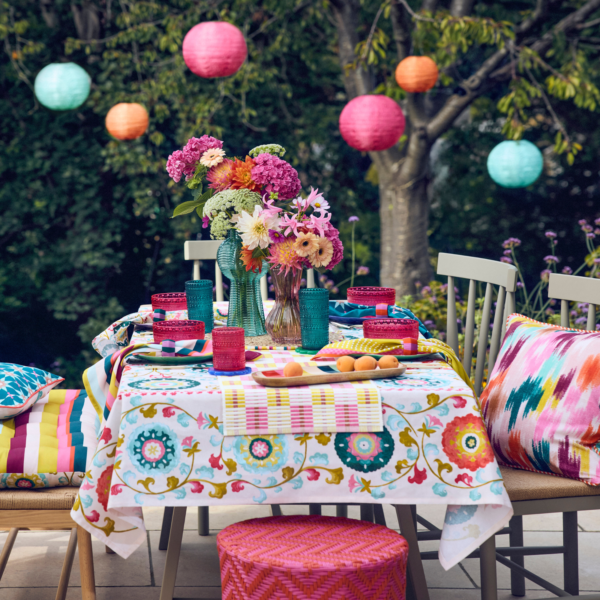 Colourful paper lanterns above a garden table decorated with coluful flowers, vases and tablecloth