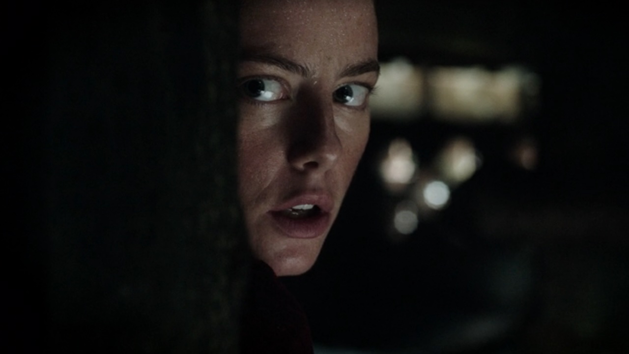 Kaya Scodelario peering around a corner looking scared in Crawl