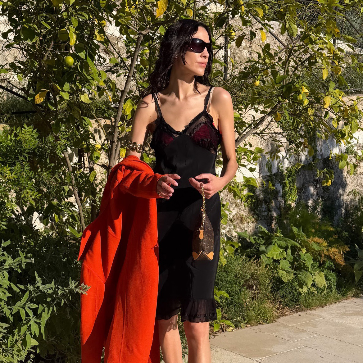 Alexa Chung wearing a red trench with a black slip dress, Louis Vuitton bag, and leopard-print Alaia thong high-heel sandals in France