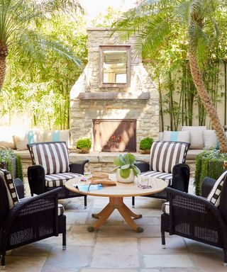 An outdoor living area with black rattan chairs with black and white striped cushions surrounding a round wooden table
