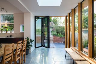 Black framed bi-fold doors looking out onto a small paved area from dining room/kitchen extension with wooden benches and other accents