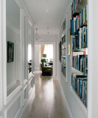 White hallway with built in shelving books mirrored panels suspended spot lighting wooden flooring leading to living room
