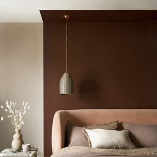 bedroom with chestnut coloured walls blush pink velvet upholstered bed and coffee coloured bedlinen