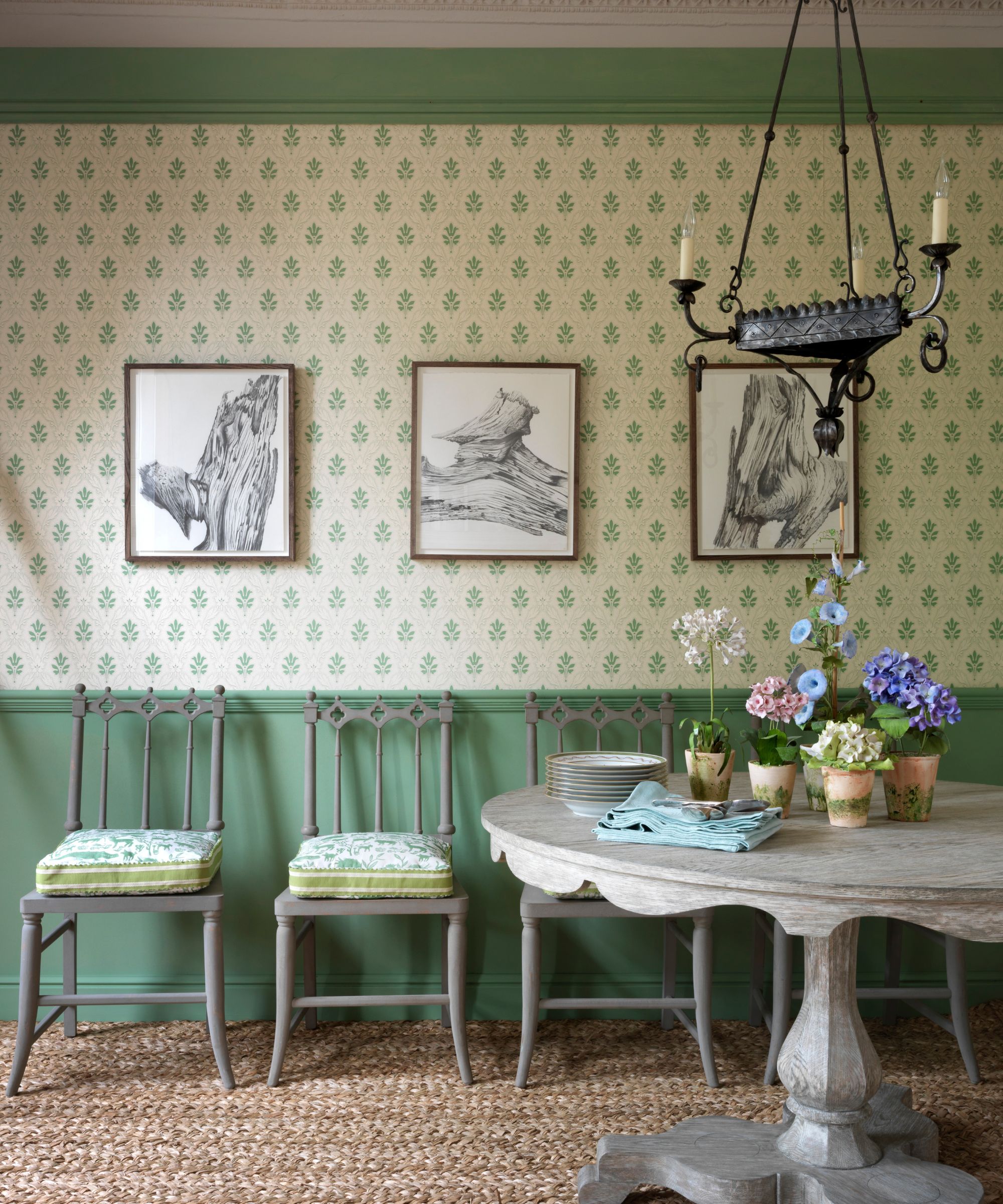 Entryway with vintage wallpaper, green ceiling trim and panelling and round wood table with plants and flowers with iron candelabra