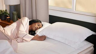A woman with long black hair sleeps on her side on the DreamCloud Luxury Hybrid mattress