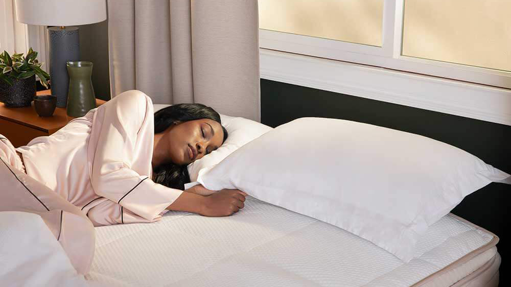 A woman with long black hair sleeps on her side on the DreamCloud Luxury Hybrid mattress