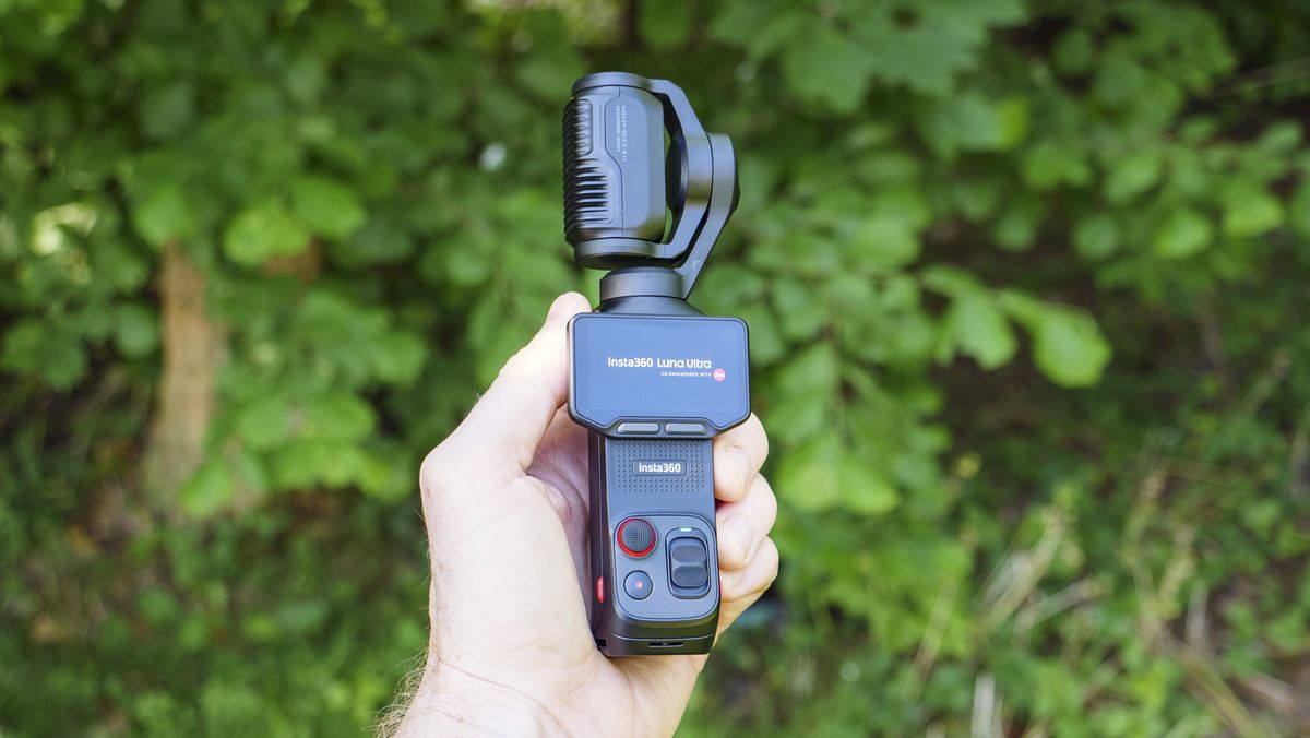 Insta360 Luna Ultra vlogging camera in person's hand, screen rotated, leafy background